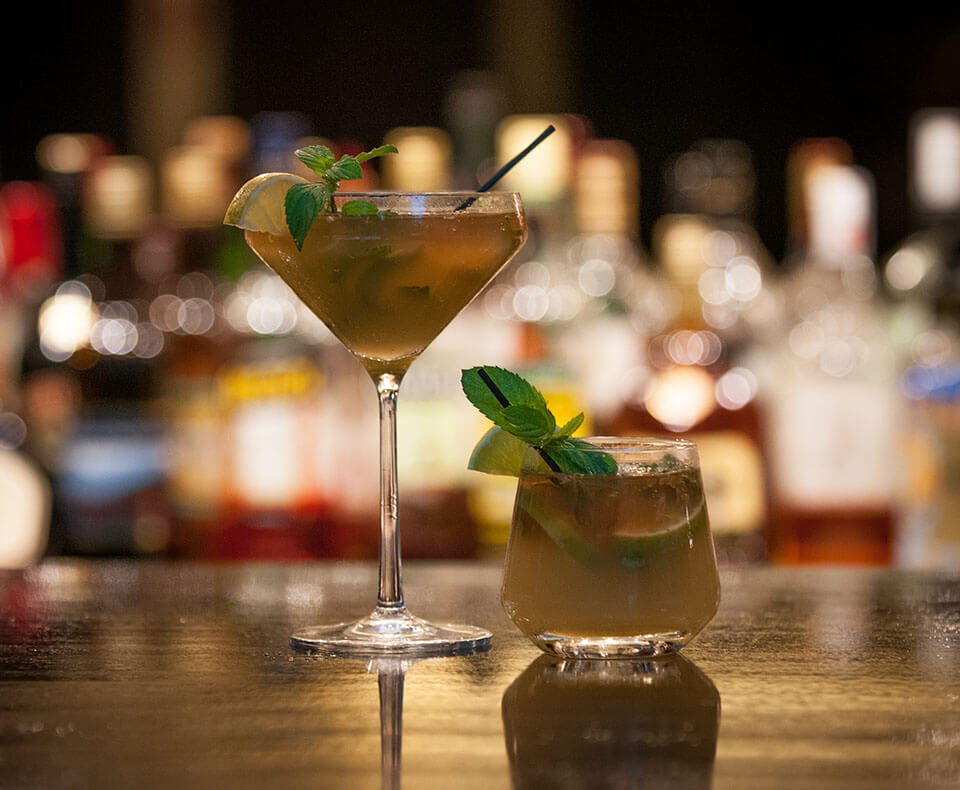 Drinks with fresh mint and lemon garnishes on bartop with soft mood lighting