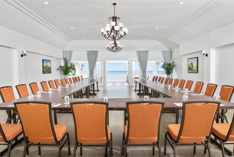 a long table with chairs and chandeliers in a room with a view of the ocean