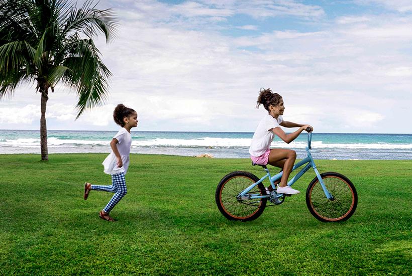 two girls on a bicycle running on grass by the ocean